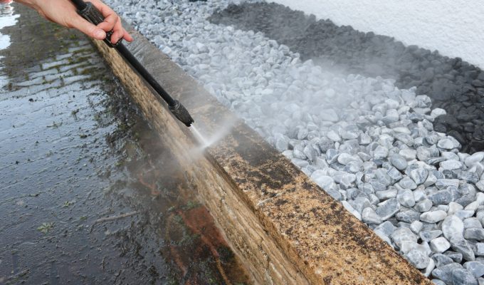 Worker is spraying water to clean the dirty wall with a water je